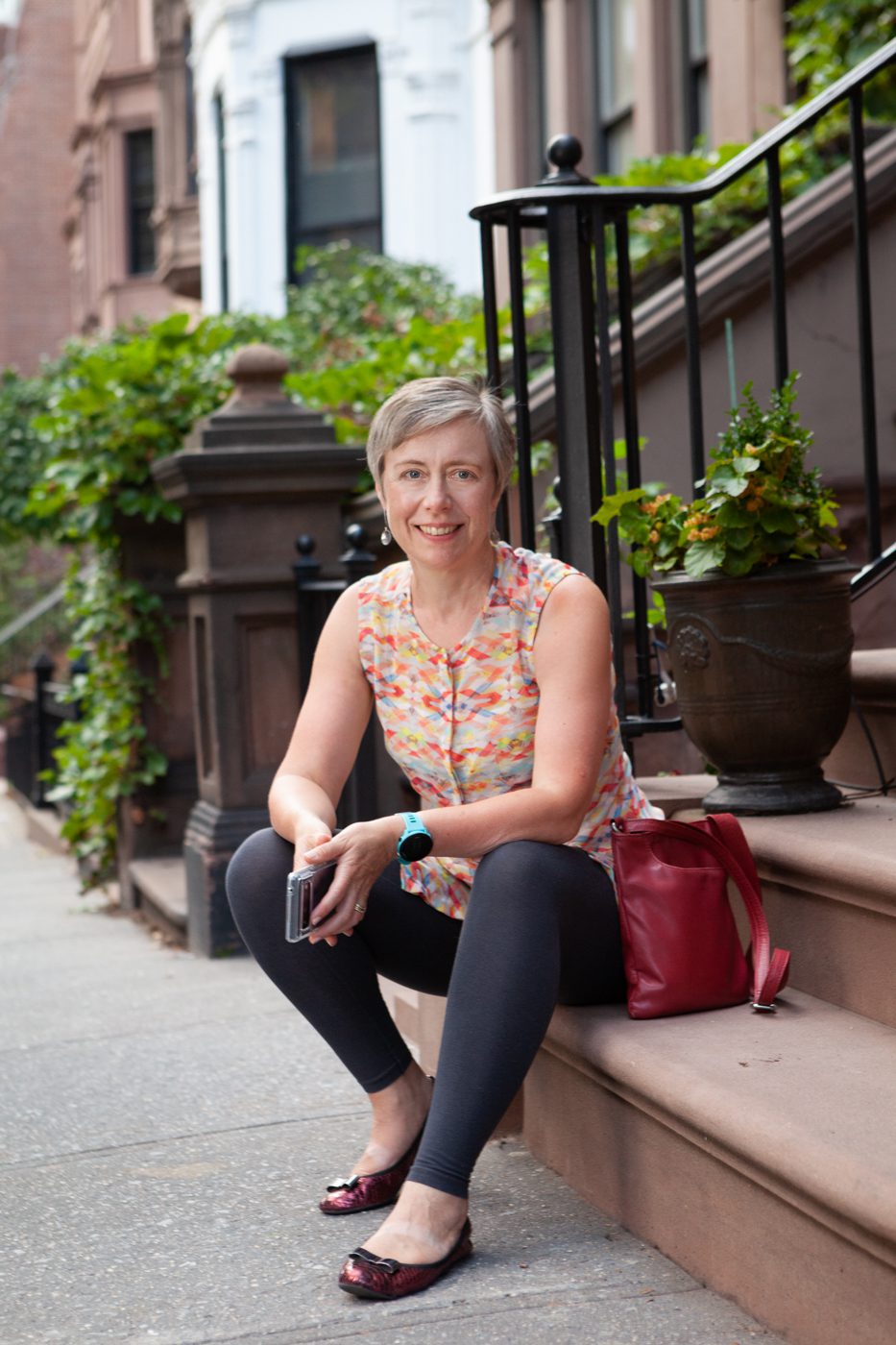 Portrait of Rebecca Maxwell, Founder, Perception Insights Ltd, sitting on a step & wearing orange shirt & black leggings